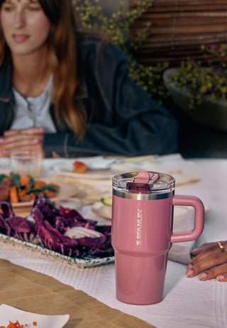 Pink Stanley tumbler with a handle on a dining table set for a meal, with a person sitting in the background.