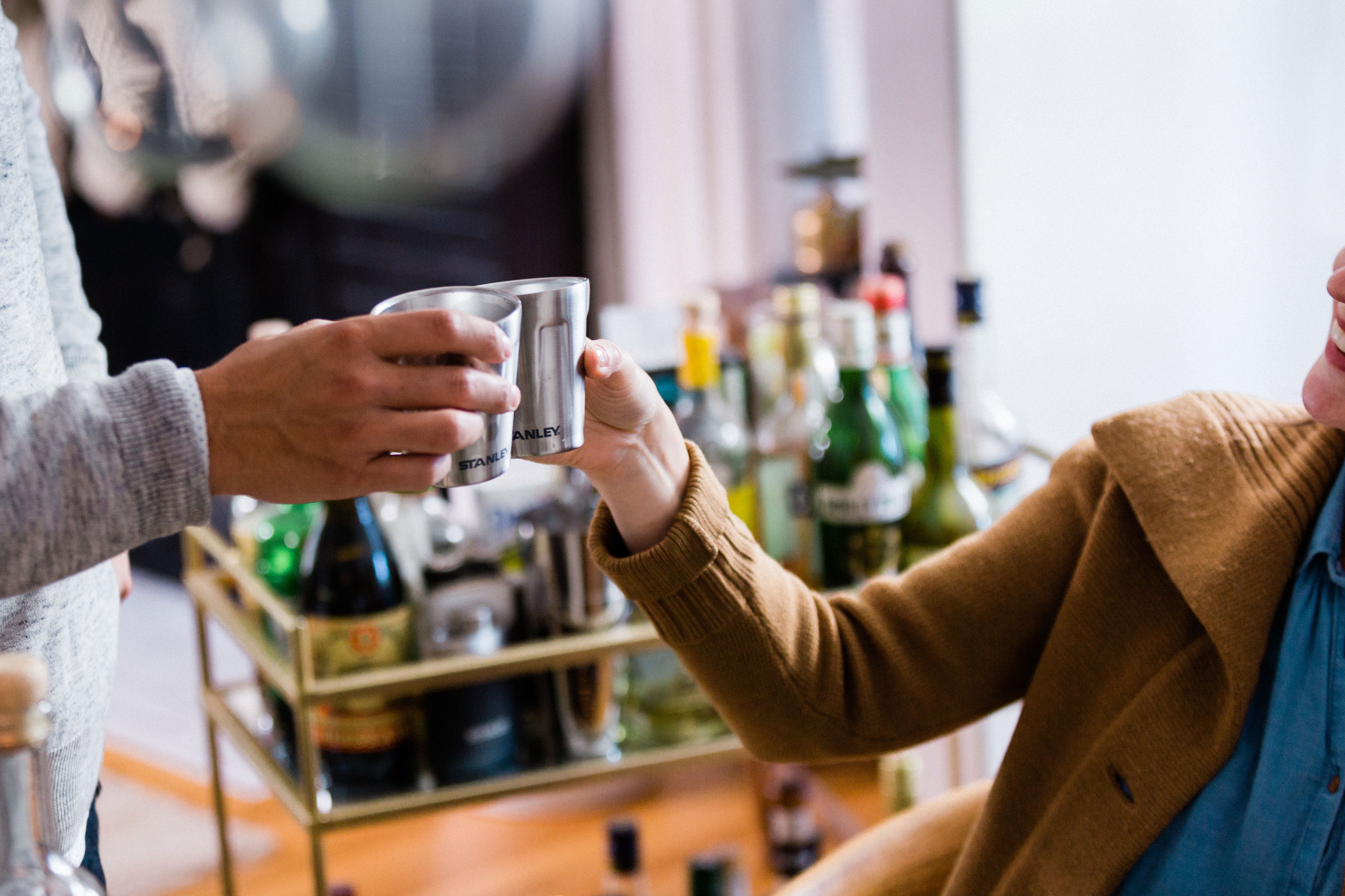 Man and woman next to a bar cart toasting with Stanley stainless-steel shot glasses.