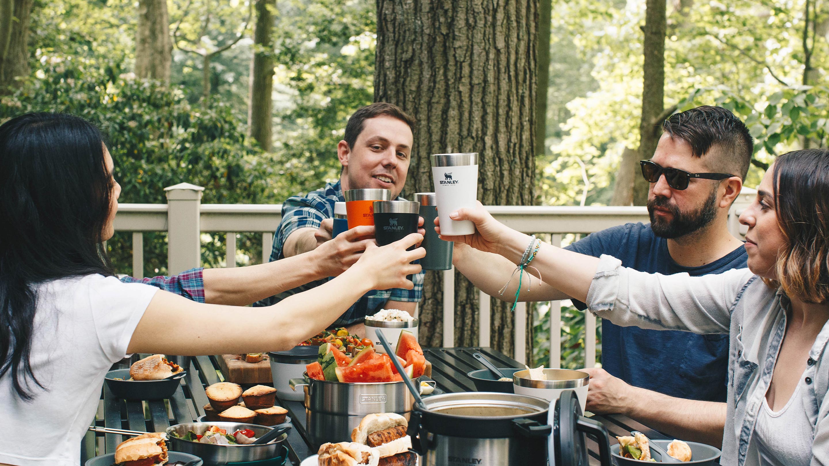 Five friends gathered at a table outside, raising their Adventure Beer Pints in a toast.