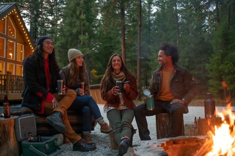 A group of adults sitting around a campfire, smiling. 