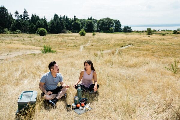 Two campers sitting around a picnic in a field.