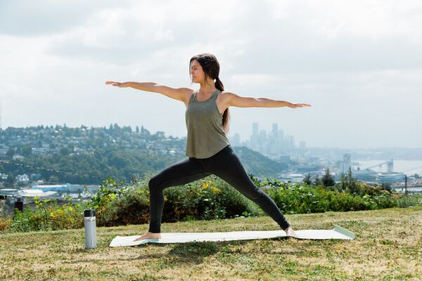 A person stands in a yoga warrior 2 pose in a natural environment with an urban landscape in the background.