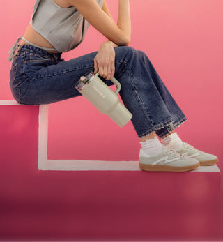 Woman sitting against a pink background holding a Stanley ProTour 40 oz Tumbler in green with handle and straw lid