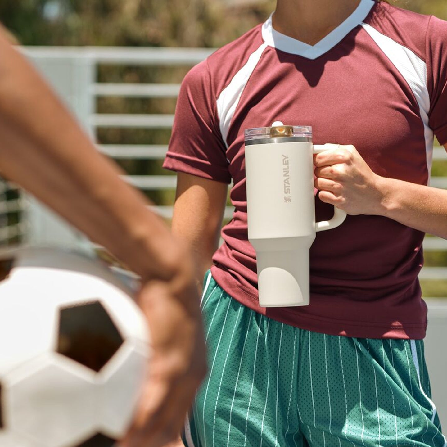 Stanley 1913 cream tumbler with handle held by soccer player in maroon jersey, soccer ball in foreground