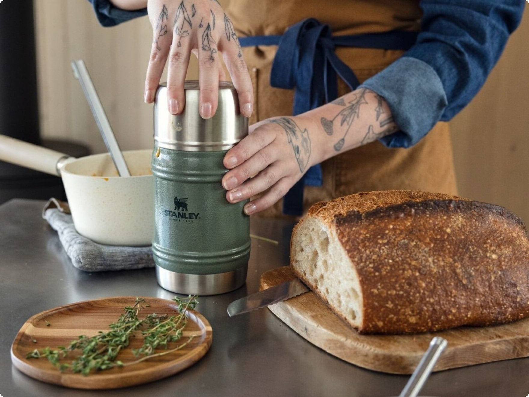 Stanley 1913 Hammertone Green food jar on a kitchen counter beside fresh sourdough bread and thyme sprigs.