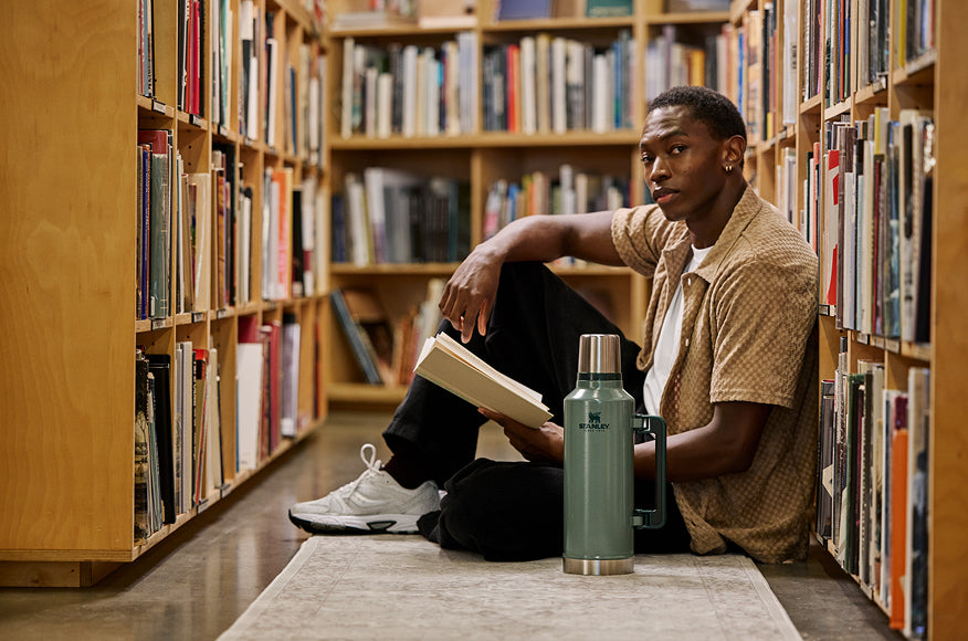 Stanley 1913 green Classic Legendary Bottle beside a young man reading in a library aisle